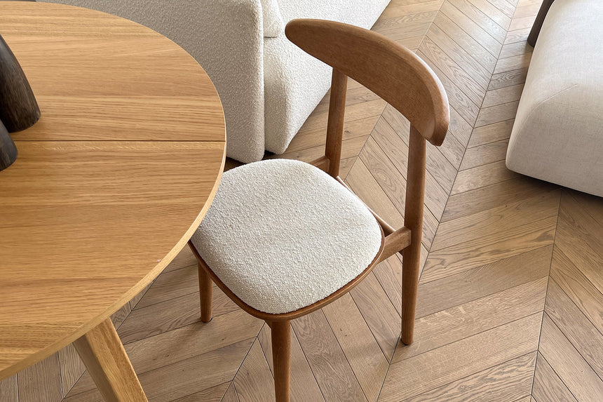 Zbliżenie na jasne tapicerowane krzesło przy okrągłym drewnianym stole.